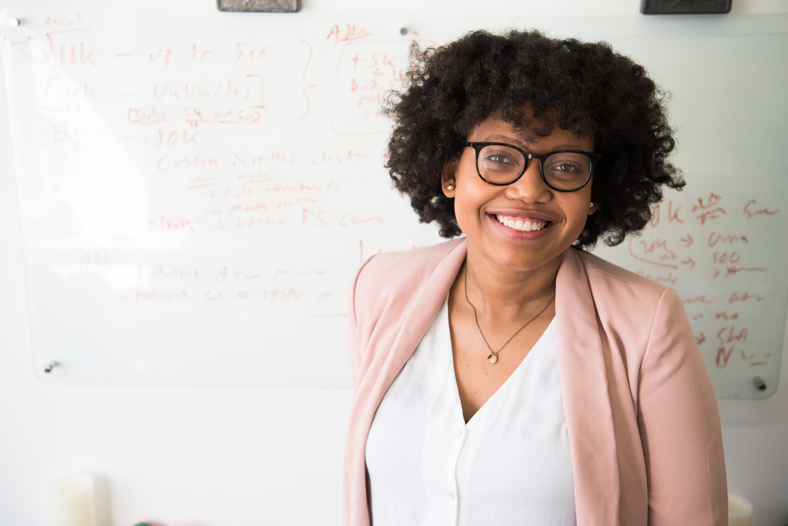 Female, African-American Professor smiles in front of a whiteboard covered with mathematical notations