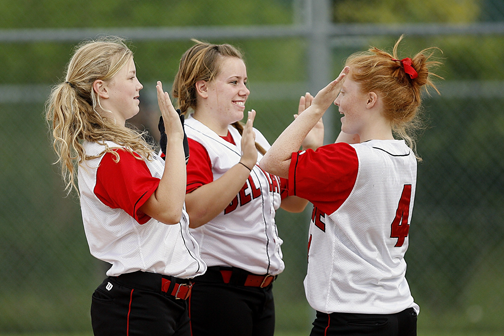 Three teen girls wearing softball uniforms exchange high-fives