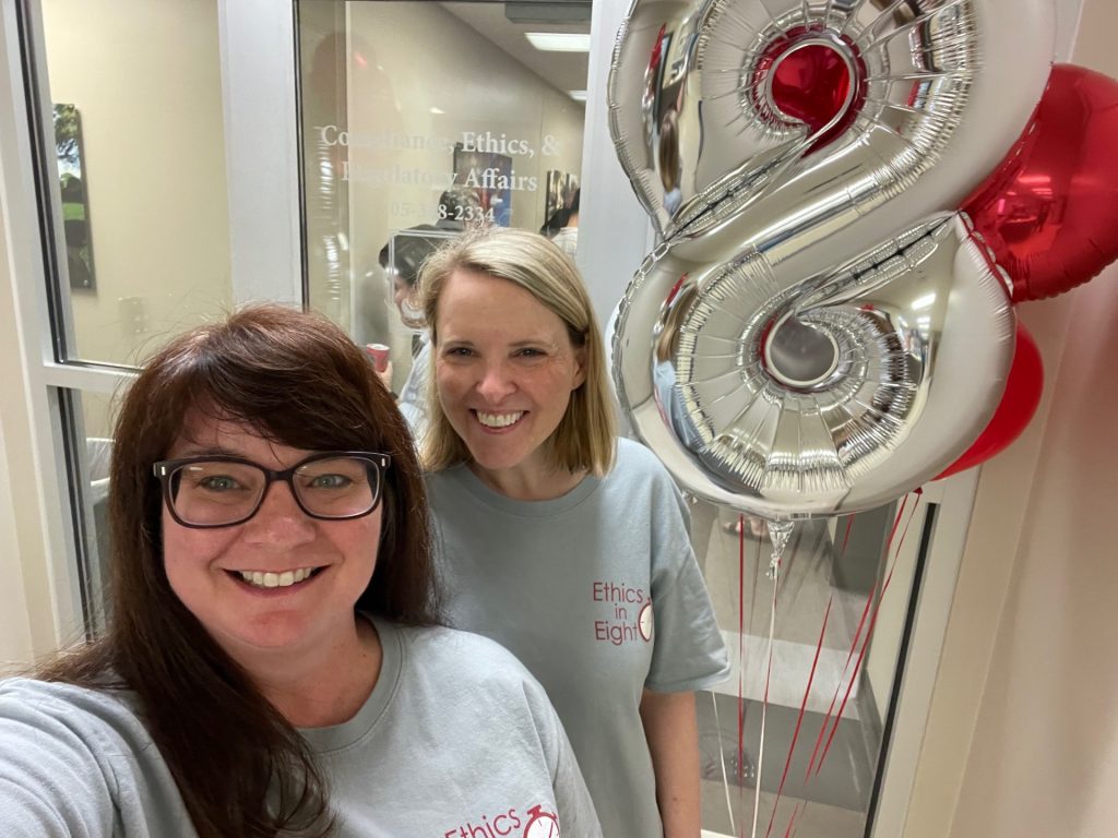Susan Reynolds and Rebecca Minder are smiling next to a metallic balloon in the shape of an 8 in the entrance to the Office of Compliance, Ethics, and Regulatory Affairs.